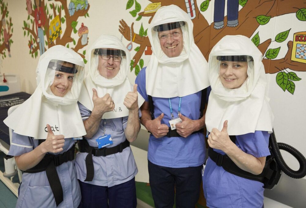 Healthcare workers wearing protective gear, thumbs up.