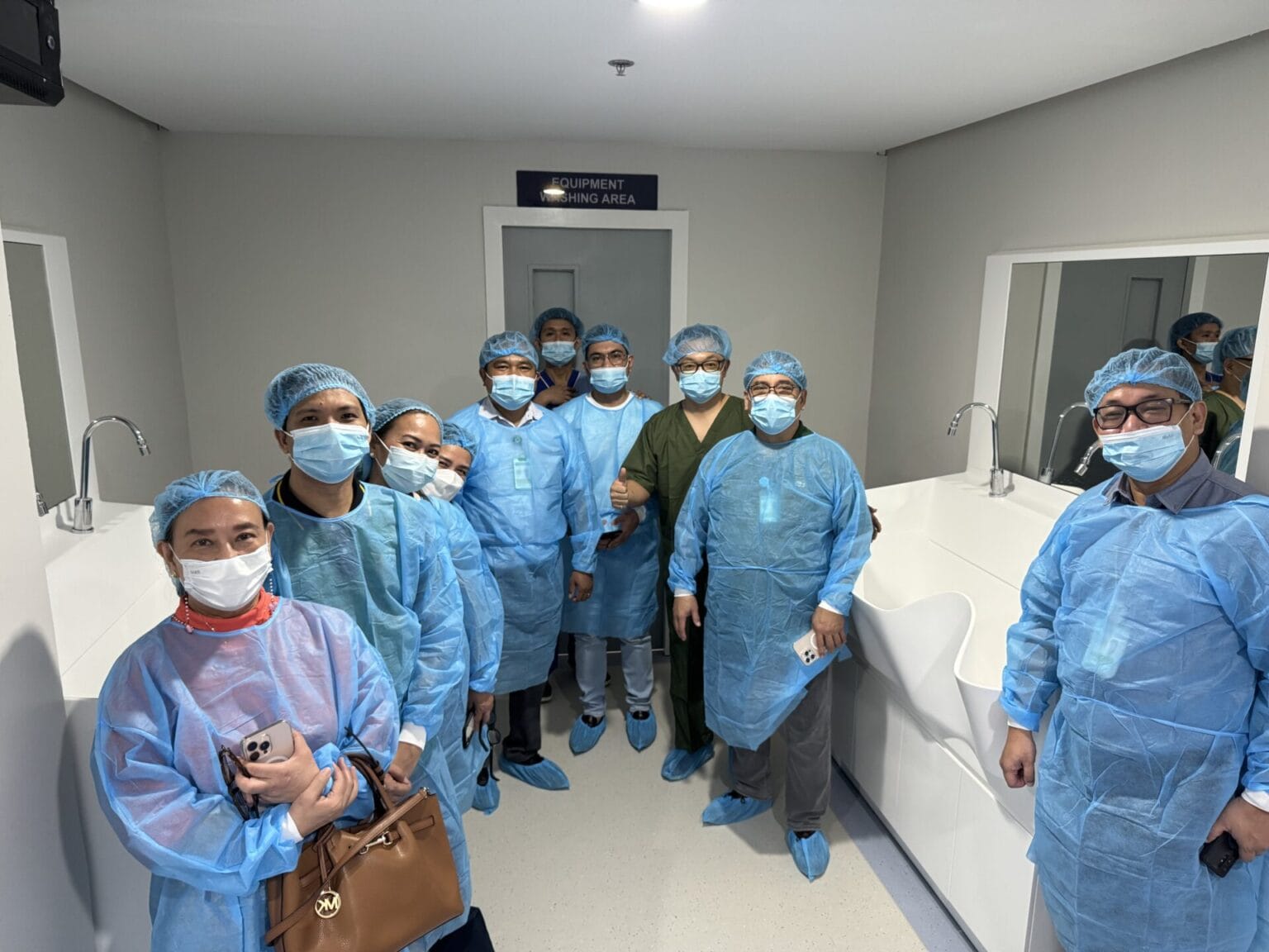 Visiting clinicians in gowns gathered beside the solid surface surgical sink at JBLMGH, Philippines