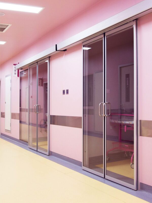 Pink-hued hospital corridor with glass doors.
